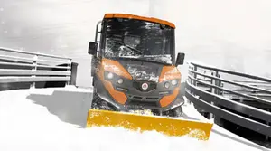 Elektrisches Arbeitsfahrzeug mit Schneepflug räumt Schnee auf einer Straße