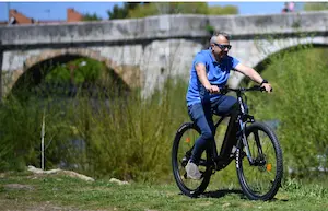 Mann fährt auf einem E-Bike der Marke UrbanBiker unter einer Brücke in grüner Natur