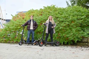 Ein Mädchen und ein Junge fahren im grünen Park mit E-Rollern – modernes Fahren erleben mit E-Mobilität & Fahrzeuge für Freizeit und Alltag.
