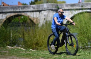 Mann fährt auf einem E-Bike der Marke UrbanBiker unter einer Brücke in grüner Natur