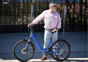 UrbanBiker E-Bikes – Person hält auf einem blauen E-Bike auf der Straße vor dunklem Glasgebäude