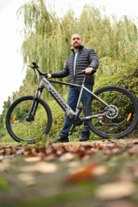 Echte Menschen. Echte Erfahrungen – Ein Mann steht mit seinem E-Bike über hartem Bodengelände