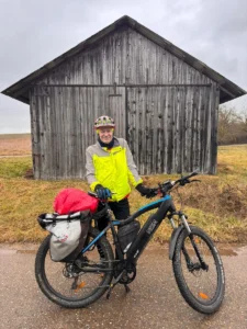 Echte Menschen. Echte Erfahrungen – Ein Mann steht vor einem E-Bike Lagerhäuschen mit seinem modernen E-Bike
